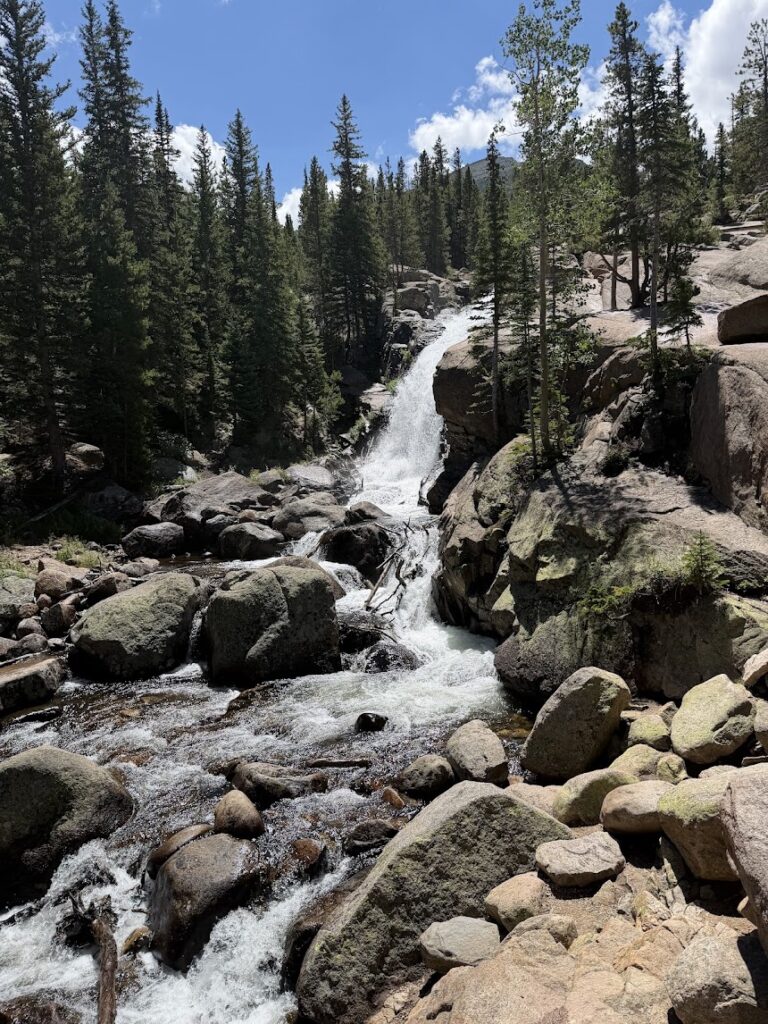 Water falling over rocks in a forested area with blue skies